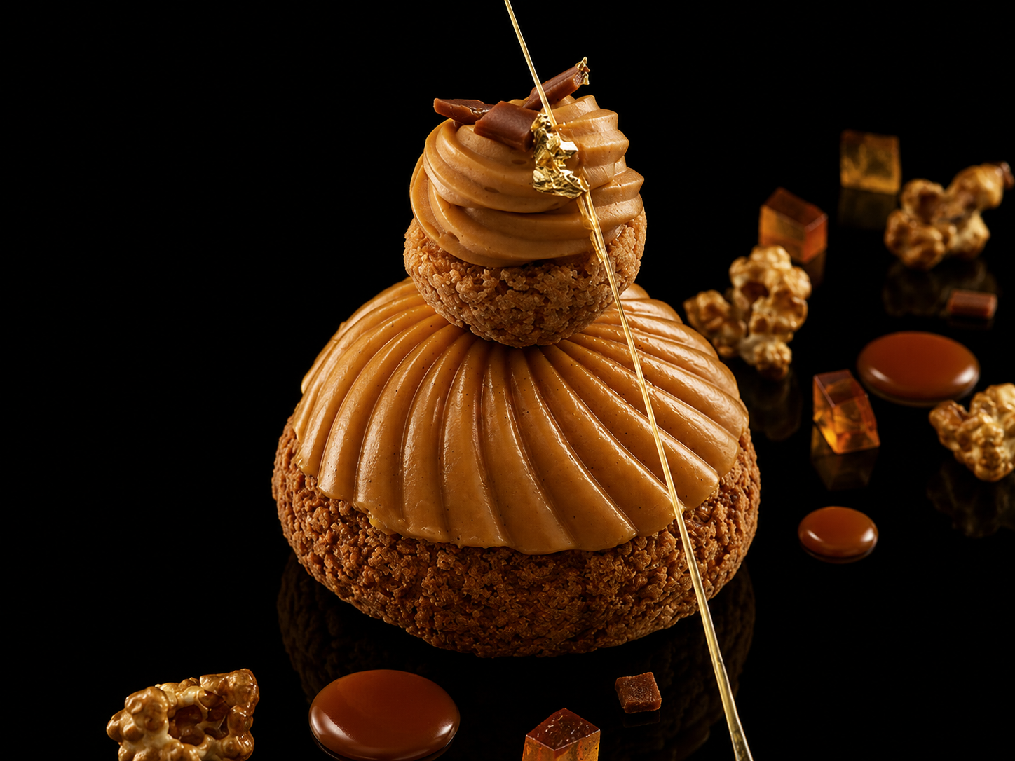 pâtisserie en forme de tour avec deux couches de gâteaux dorés et caramel, décorée d'une fine broche en or, entourée de morceaux de caramel, chocolat, et noix