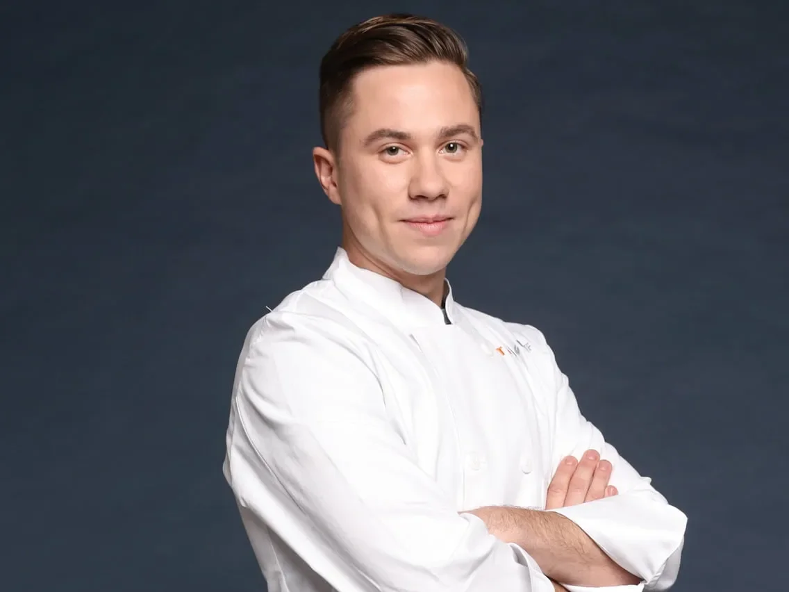 Dessert dans un bol blanc, garniture de caviar de gelée noire, poudre verte, petites fleurs blanches, et sauce claire, sur une surface de pierre.