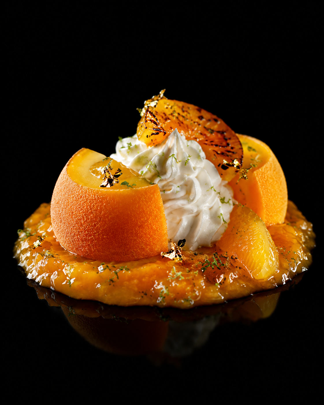 Un dessert élaboré avec des morceaux d'orange, une crème fouettée au centre, et des agrumes garnis de zestes d'or, présenté sur une surface noire réfléchissante.