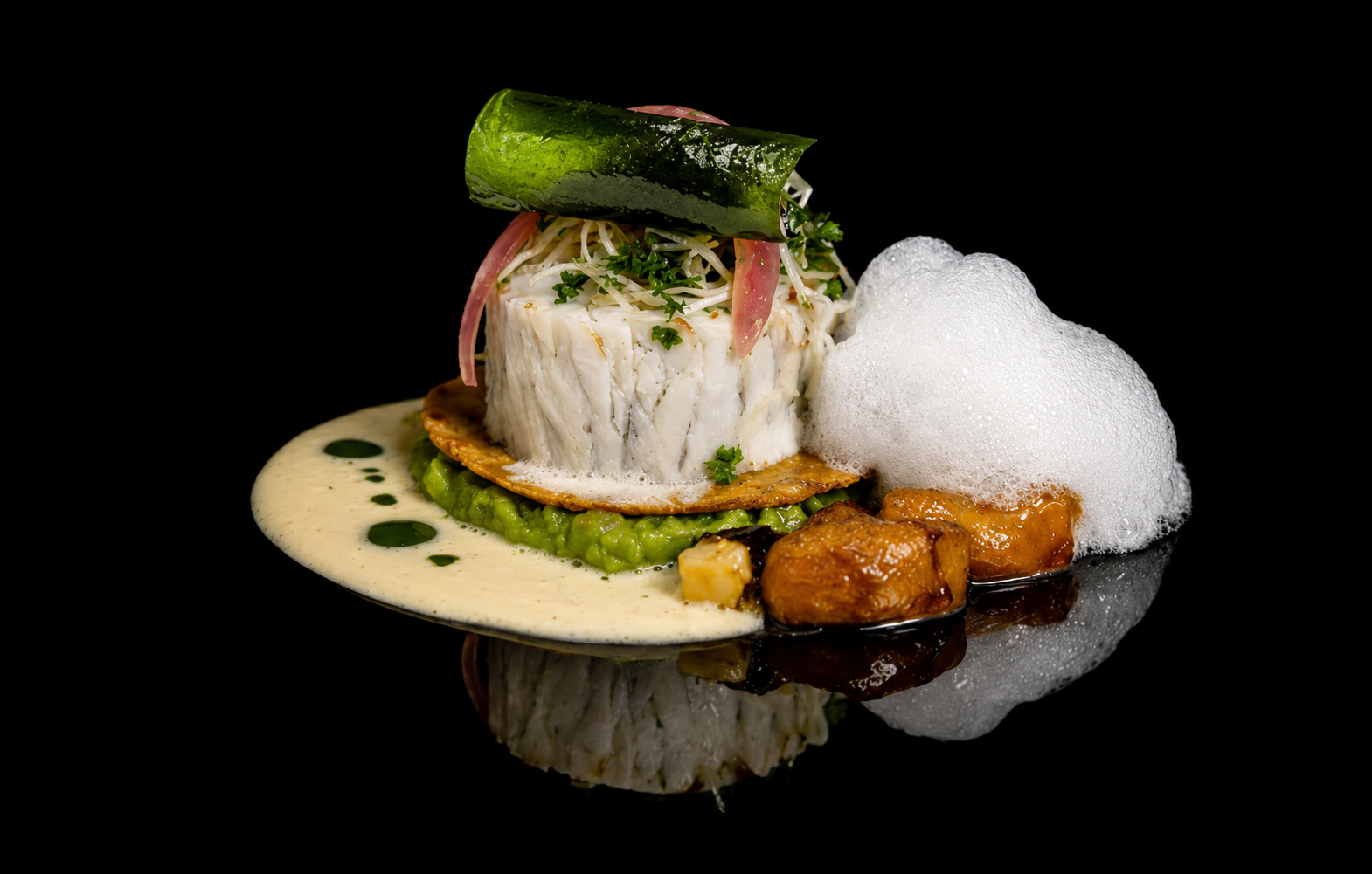 Assiette de poisson blanc avec garnitures, sauce, mousse de savon et légumes sur fond noir.