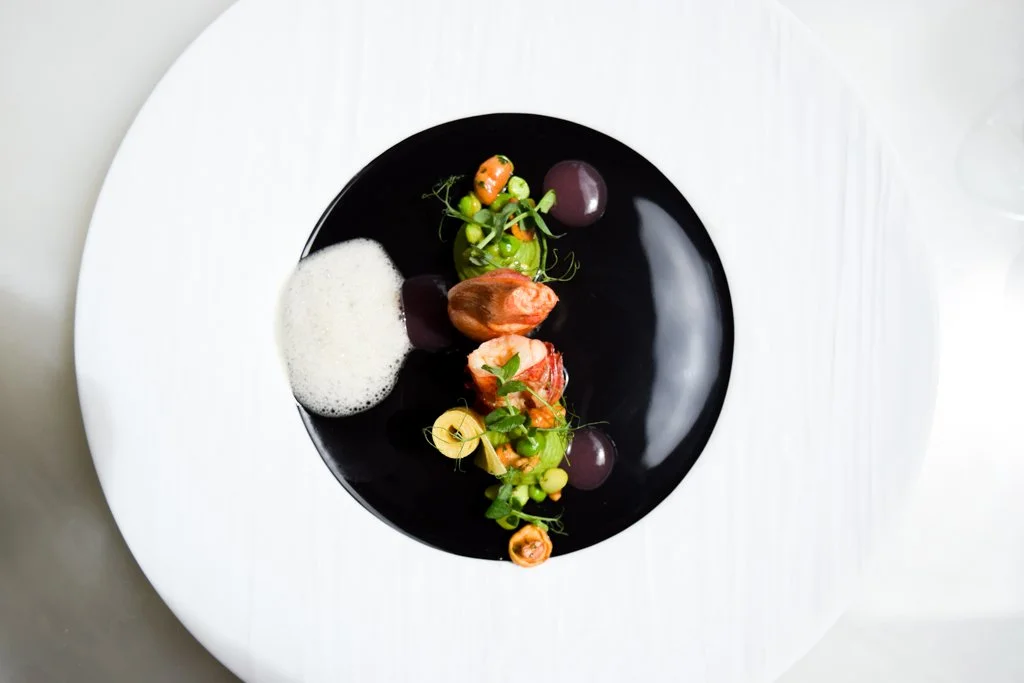 Assiette gastronomique avec fruits de mer, légumes frais, et espuma, présentée de façon élégante avec une décoration minimaliste.