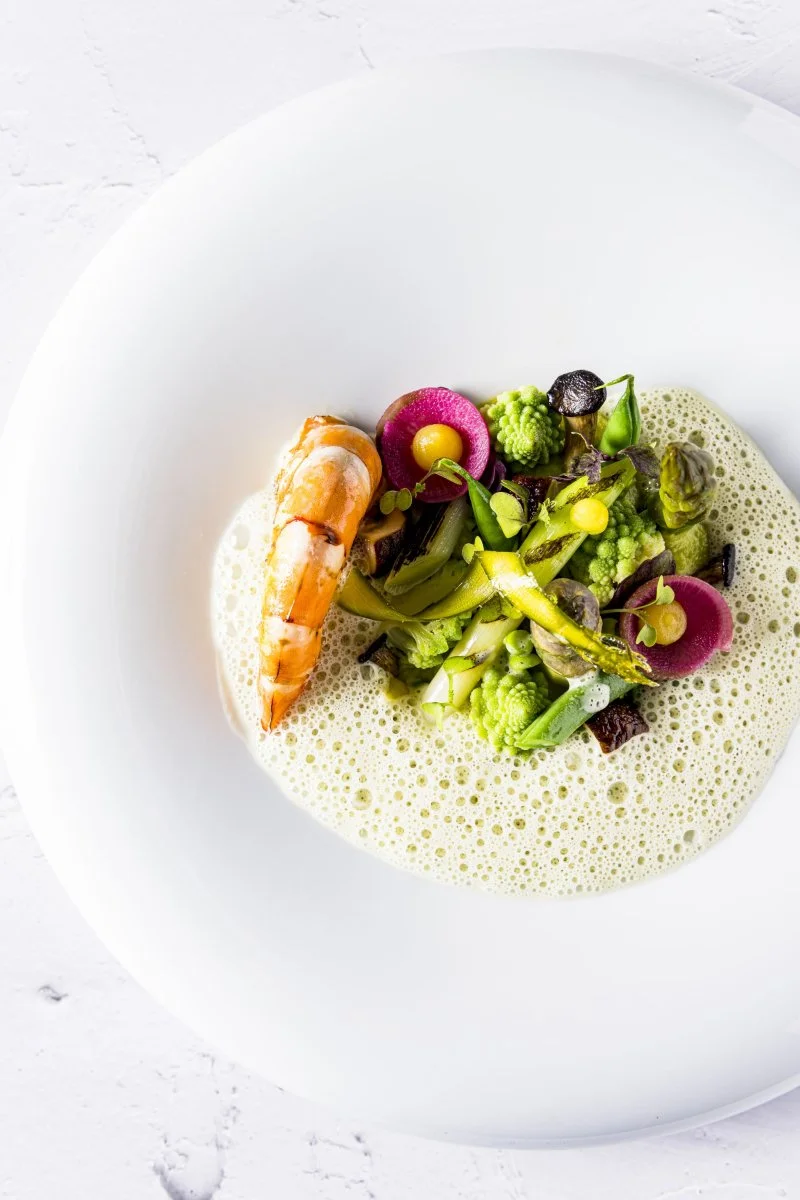 Assiette blanche contenant un plat de légumes verts variés, une crevette grillée et une mousse légère