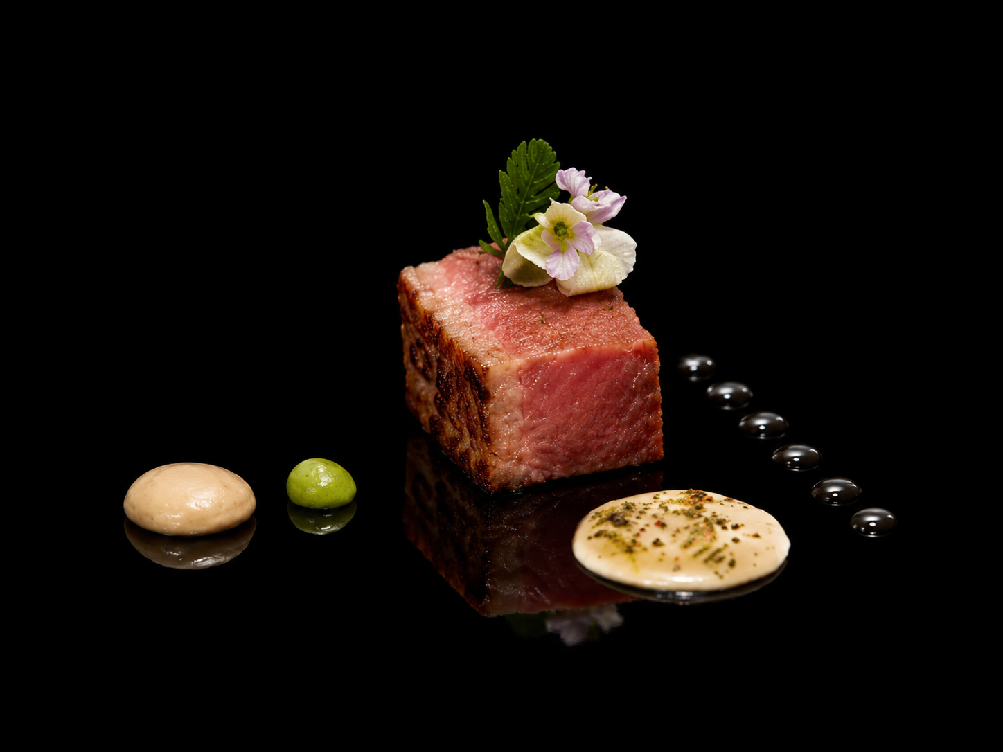 Gros plan d'un morceau de viande saignante, décorée avec des fleurs et une feuille verte, accompagnée de différentes sauces sur un fond noir.