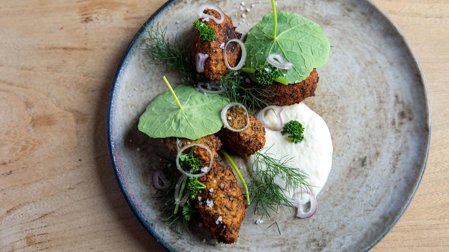 Assiette de croquettes de légumes garnies de feuilles de menthe, d'aneth, de rondelles d'oignon et de persil, avec une cuillerée de sauce blanche.