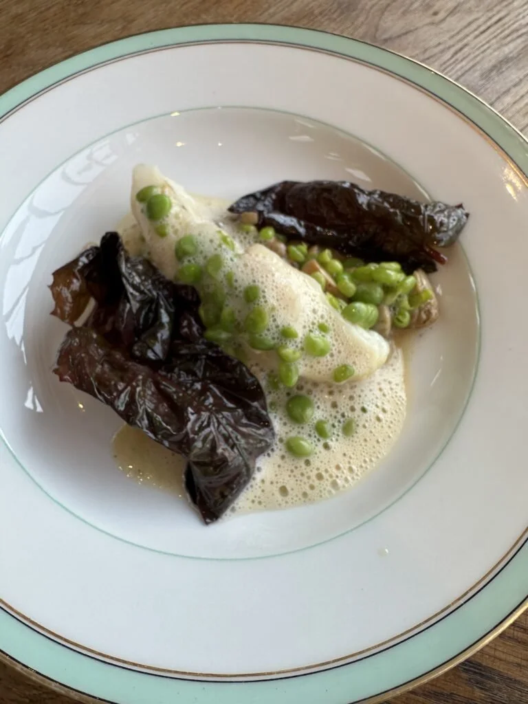 Assiette avec des feuilles d'aubergine, des pois verts, et une sauce mousseuse