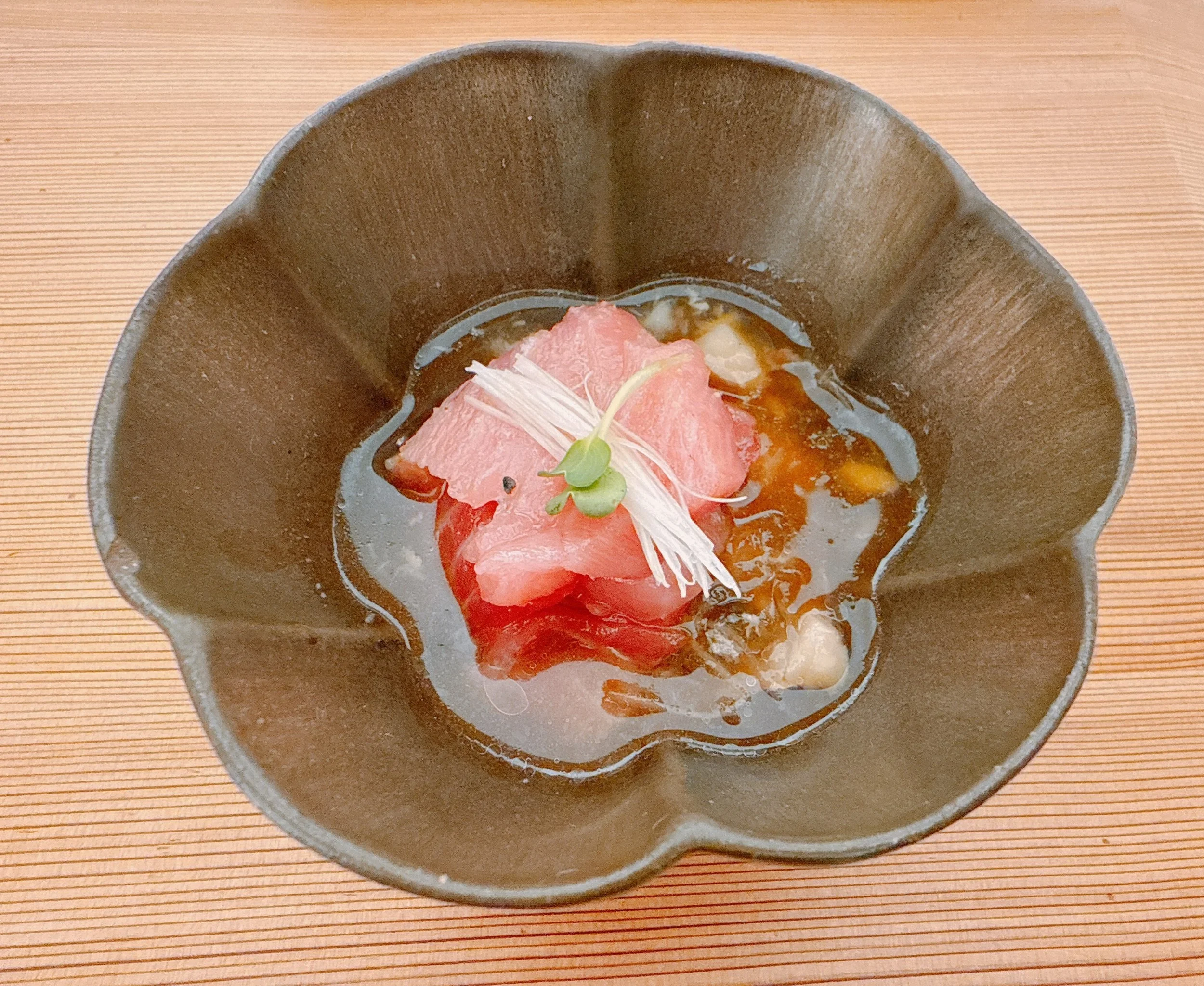 Tranches de poisson cru (sashimi) dans une sauce légère, garnies de microgreens, dans un bol en forme de fleur, sur une table en bois.