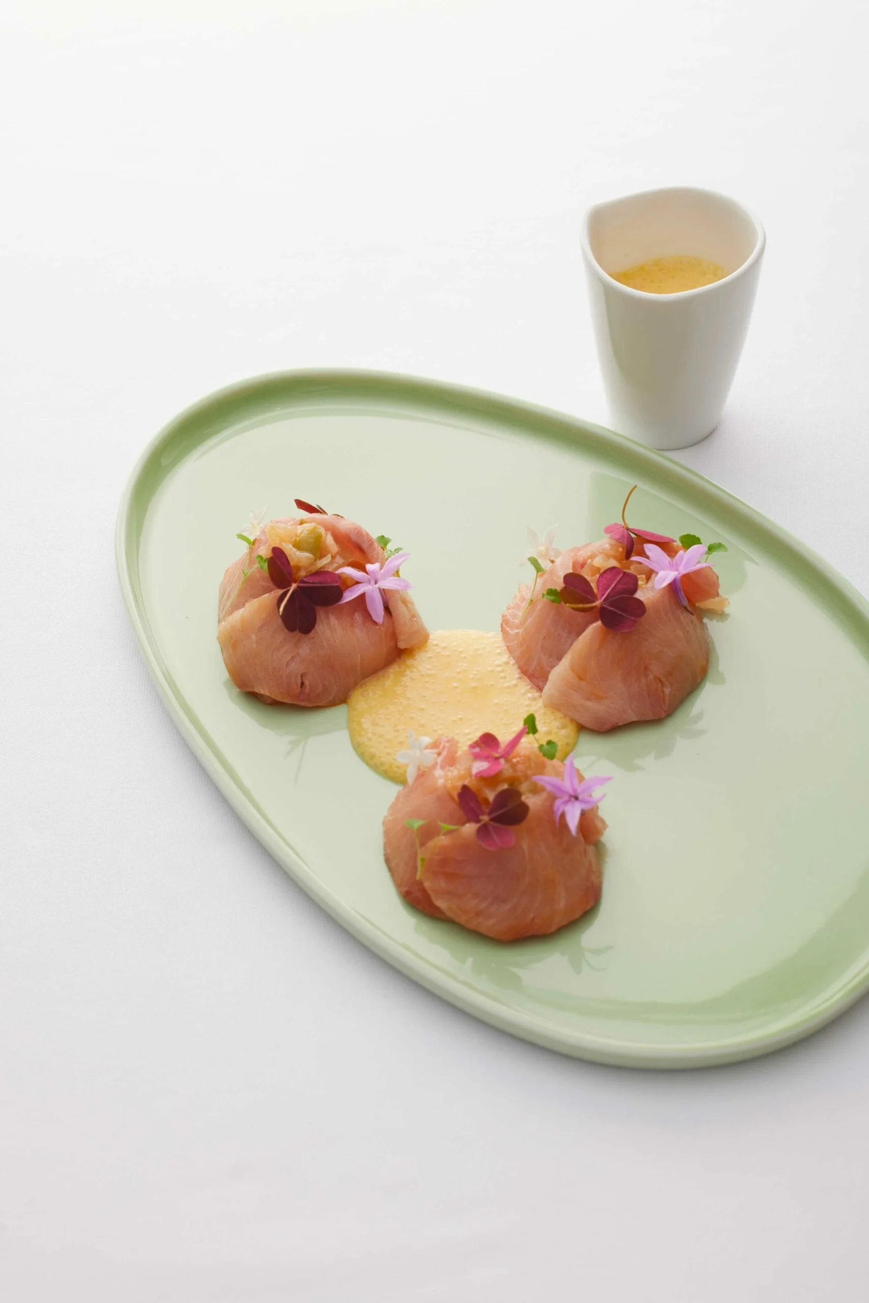 Assiette de tartare de saumon garnie de fleurs comestibles, accompagnée d'une sauce citronnée et d'une boisson dans un verre blanc.