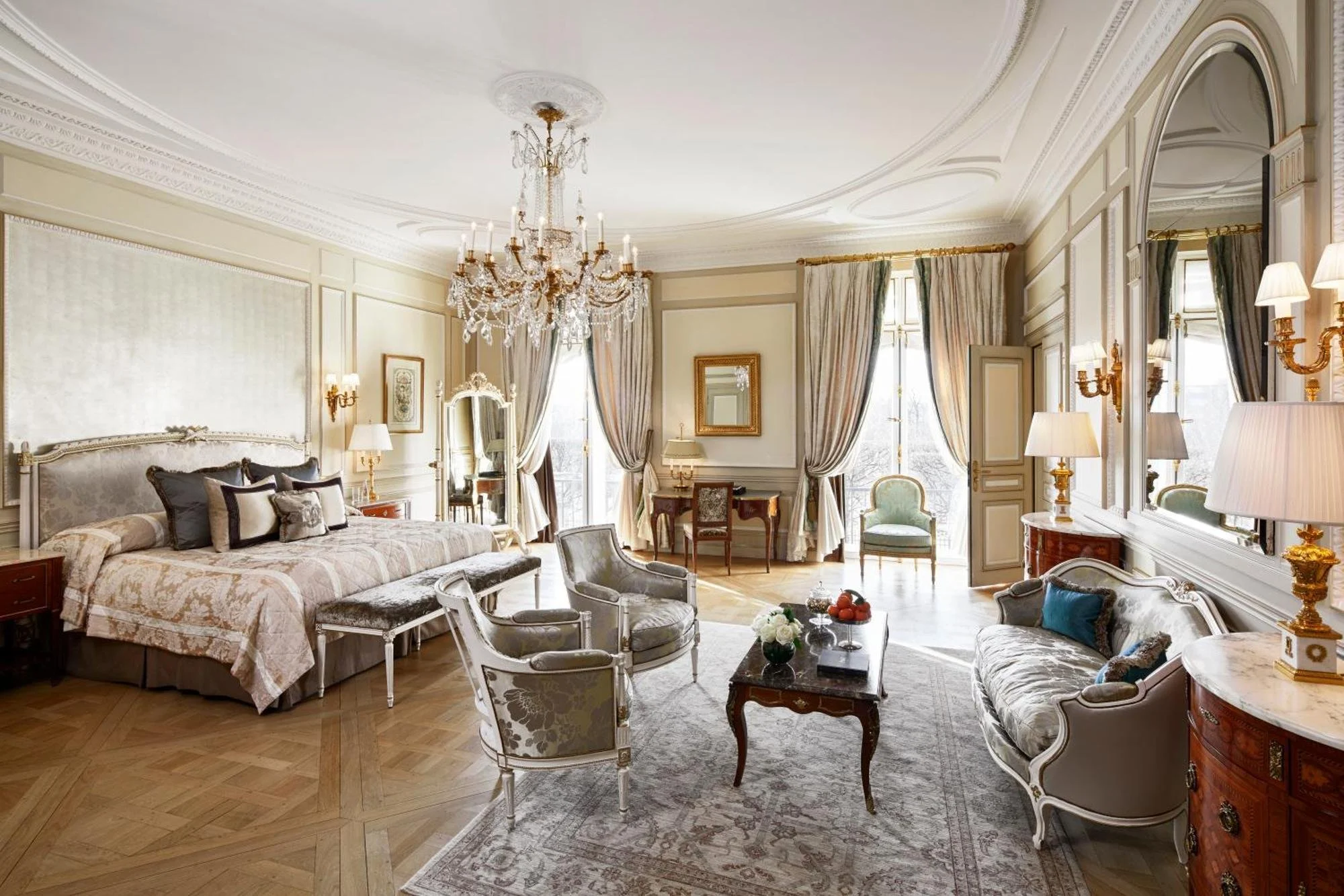 Une élégante chambre de style classique avec un grand lit à baldaquin, canapé, fauteuils, tapis, et des rideaux en tissus précieux. Décorée avec un chandelier en cristal, des lampes en laiton, et un grand miroir.