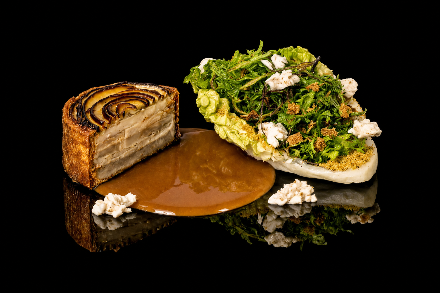 Gâteau à étages avec un motif en spirale de pommes pourries, accompagné d'une salade verte avec des morceaux de fromage blanc et de la poudre de biscuit, servi avec une sauce caramel sur une surface noire réfléchissante.