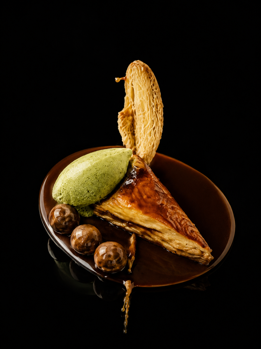 Une tarte aux pommes glacée avec une boule de glace à la pistache et quatre billes de chocolat sur une assiette en céramique
