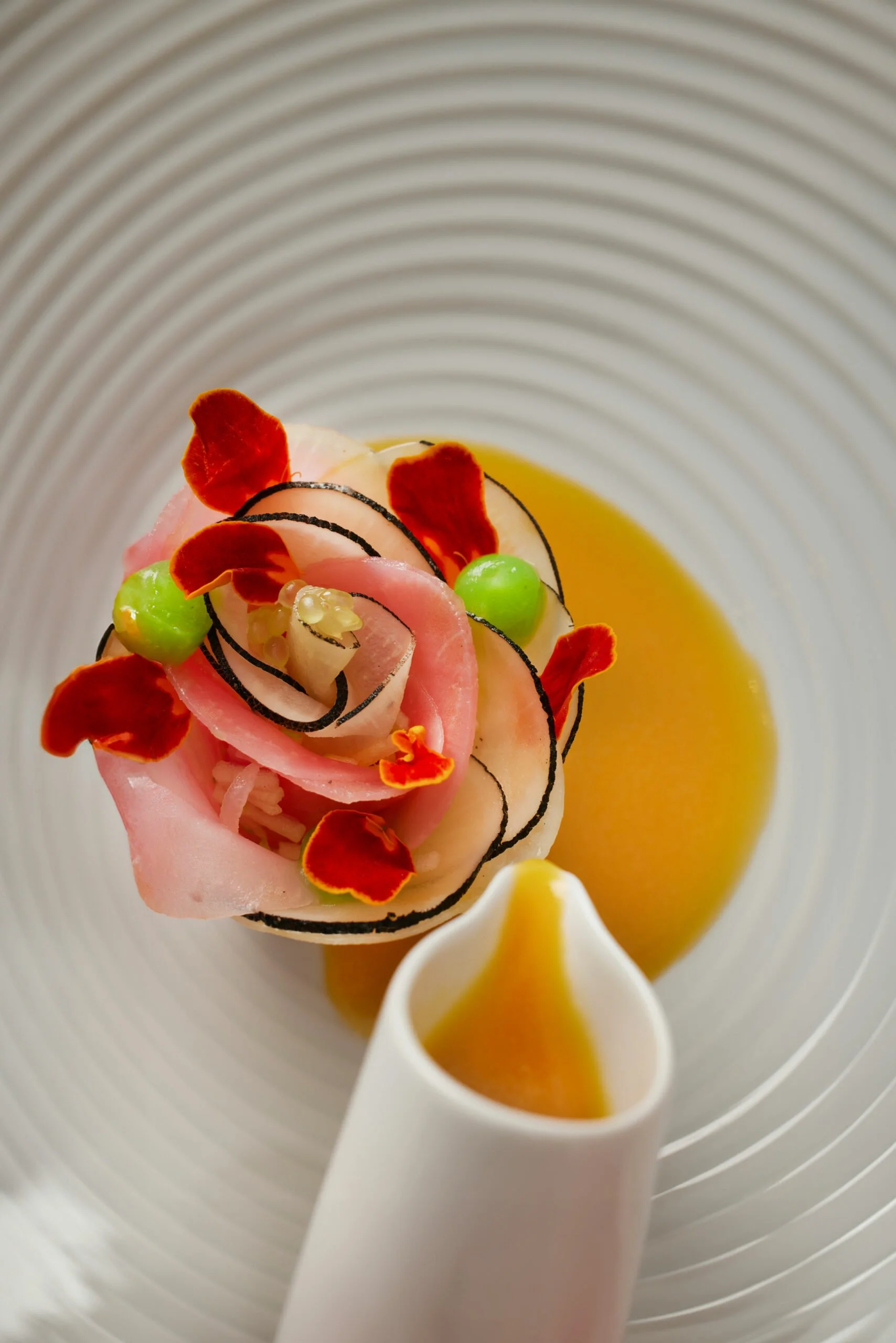 Plat culinaire avec un cygne en purée de légumes, décoré de pétales de fleurs, de légumes verts, et un filet de sauce jaune, présenté dans une assiette blanche.