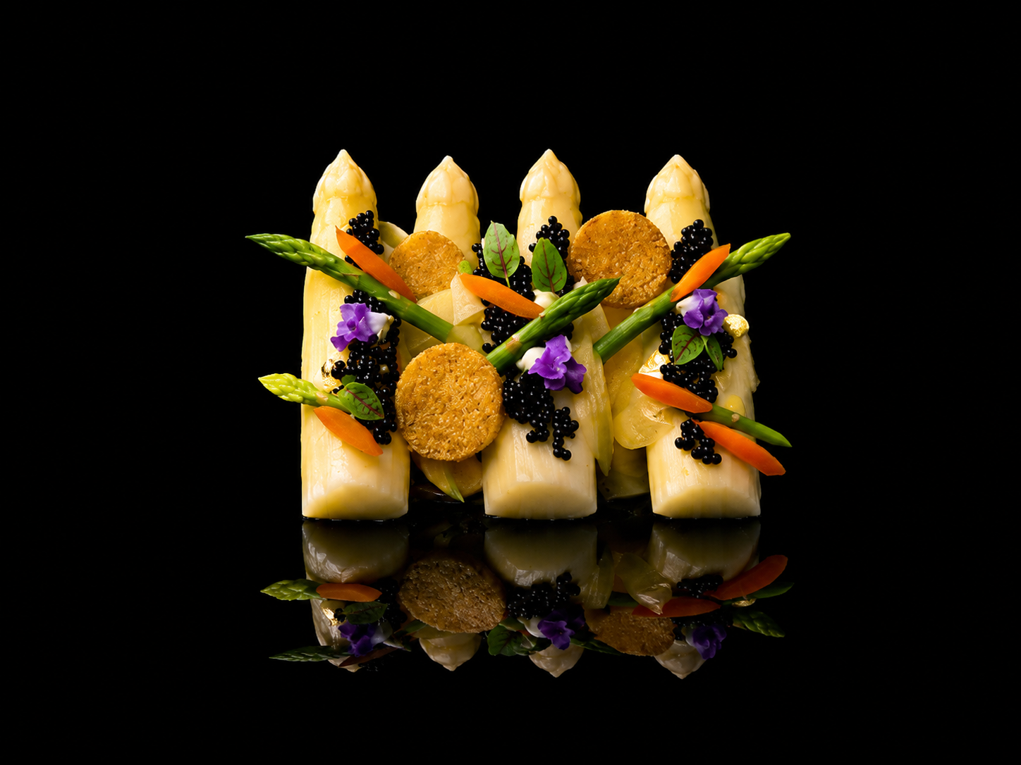 Gros plan d'une présentation culinaire sophistiquée avec des asperges, des tranches de fromage, des petits biscuits, des morceaux de carotte, des feuilles vertes, des fleurs violettes, et des grains noirs sur un fond noir