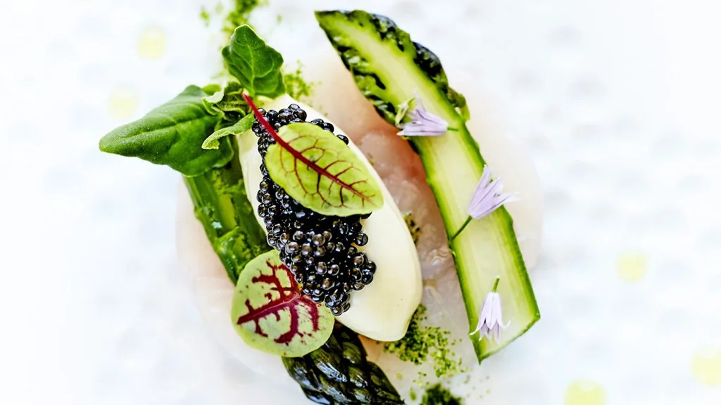 Assiette avec des légumes, des feuilles de salade, du concombre, des herbes, et du caviar noir, présentée avec des fleurs comestibles.