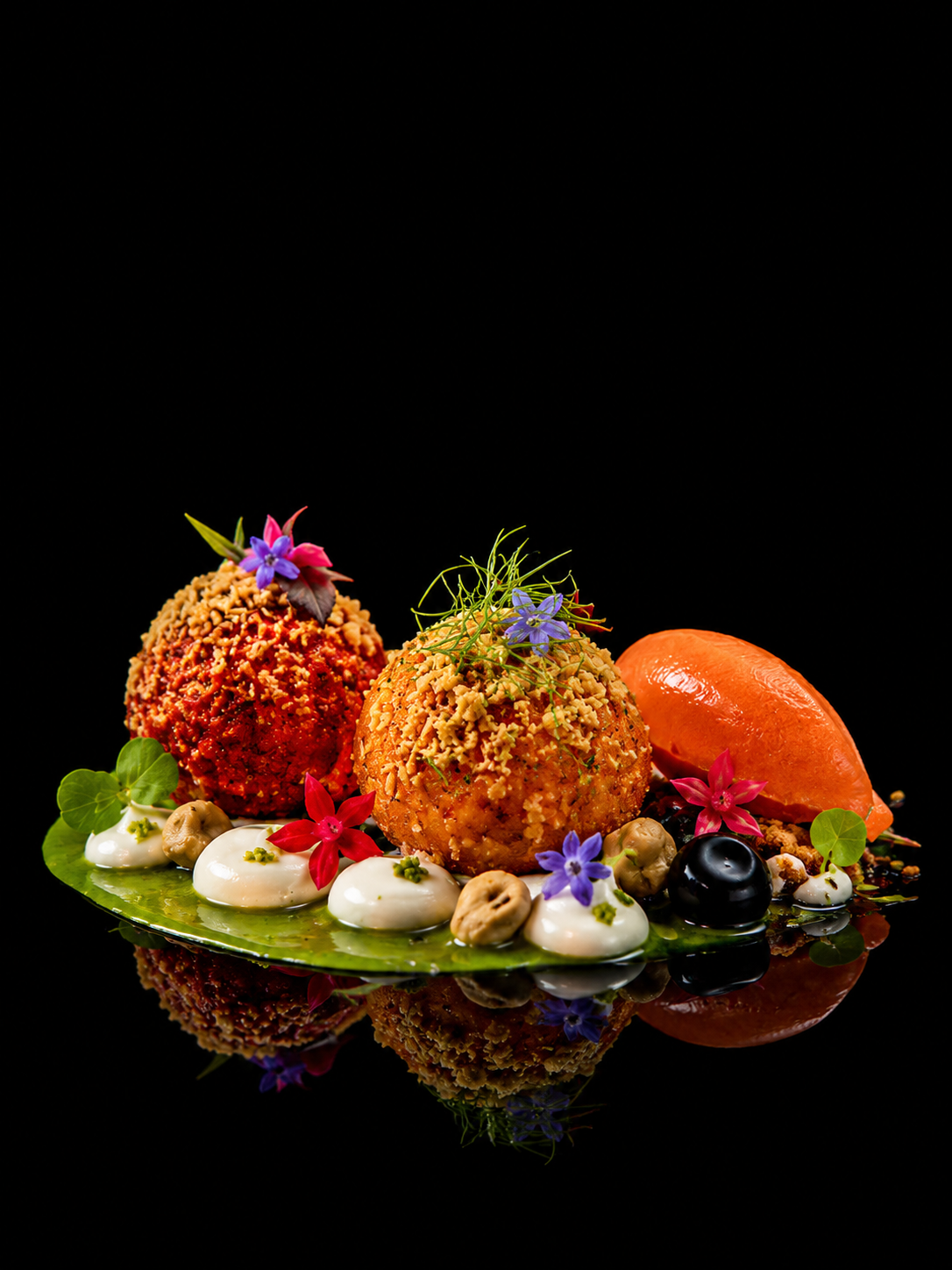 Assiette de petits falafels garnis de fleurs comestibles, légumes, sauces et noix, avec un fond noir.