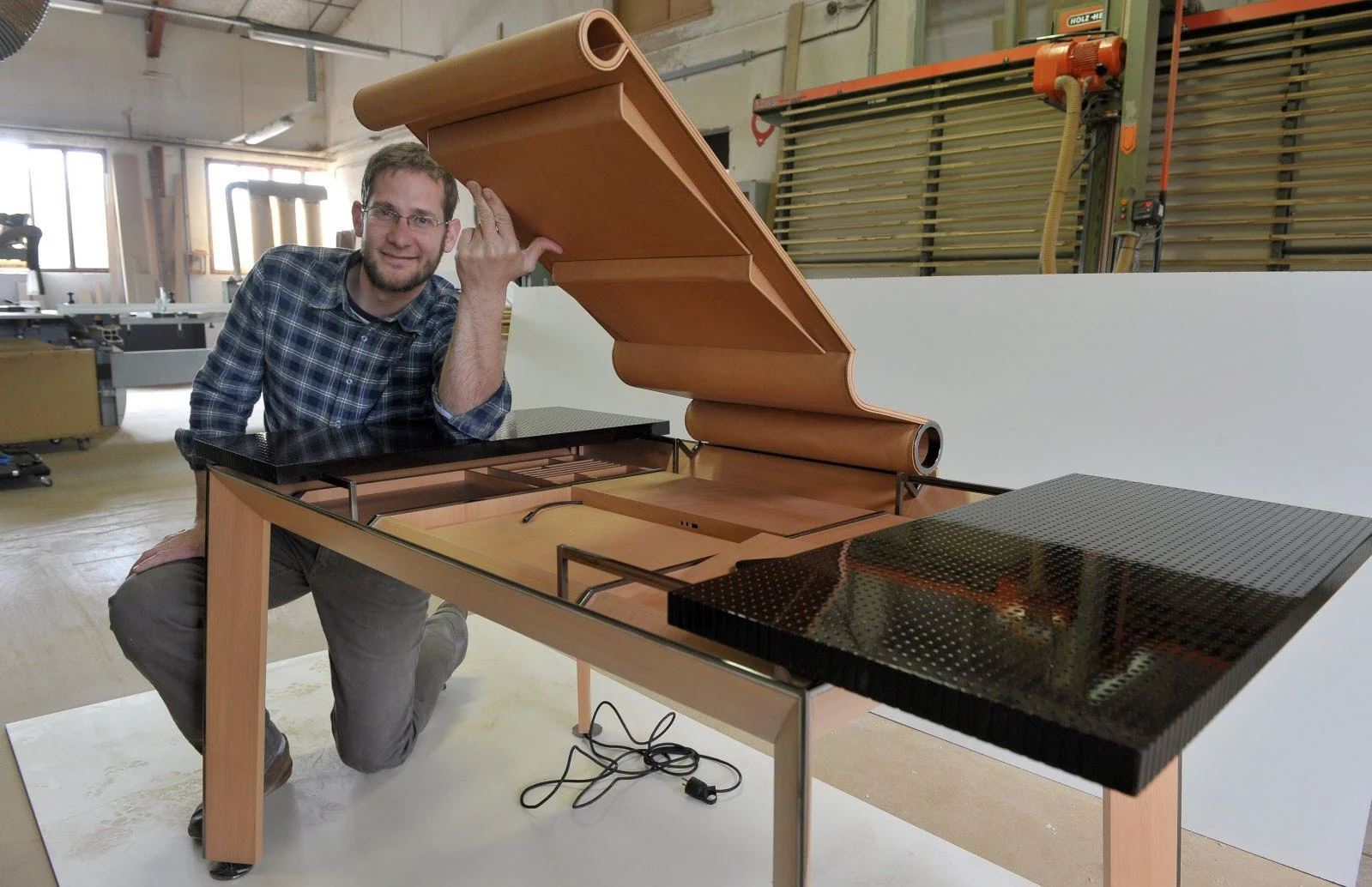 Homme posant à côté d'un piano à queue en cours de fabrication dans un atelier.