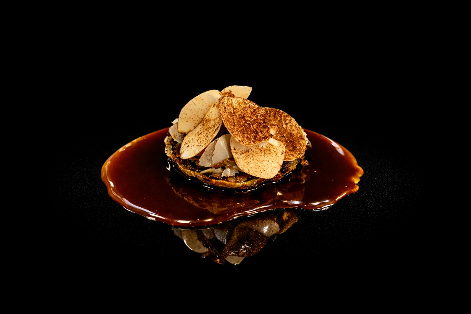 Dessert avec une sauce au chocolat, garniture de chips de banane et éclats de noix, présenté sur un fond noir.