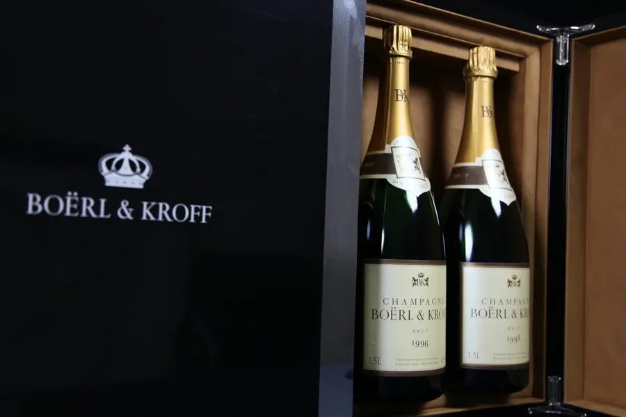 Deux bouteilles de champagne Boërl & Kroff dans un coffret en bois, à côté d'une boîte noire avec le logo et le nom de la marque.