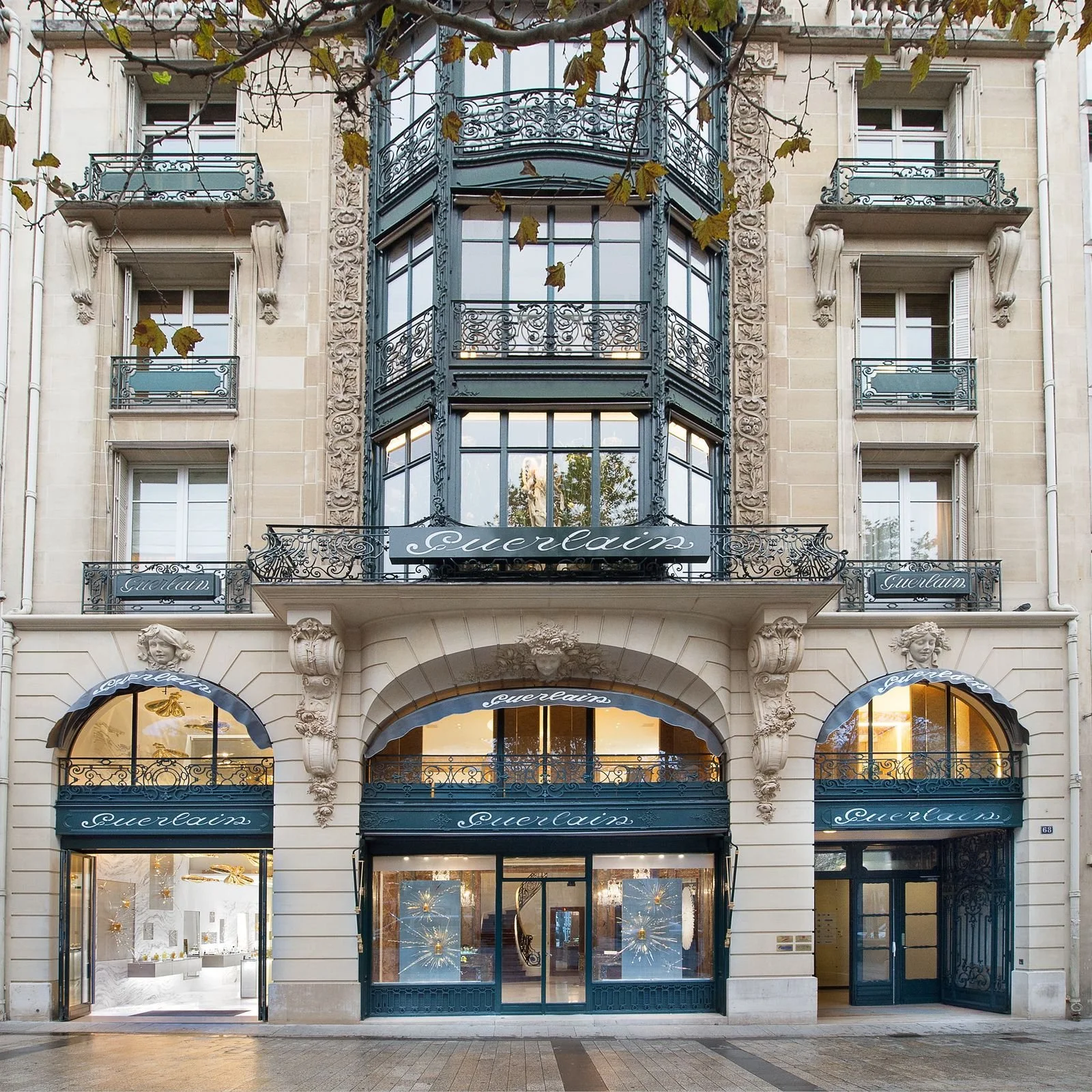 Facade d'une boutique de bijoux appelée 'Guerlain', avec des fenêtres en verre entourées de détails en architecture classique et des balcons en fer forgé, situé au rez-de-chaussée d'un bâtiment en pierre.