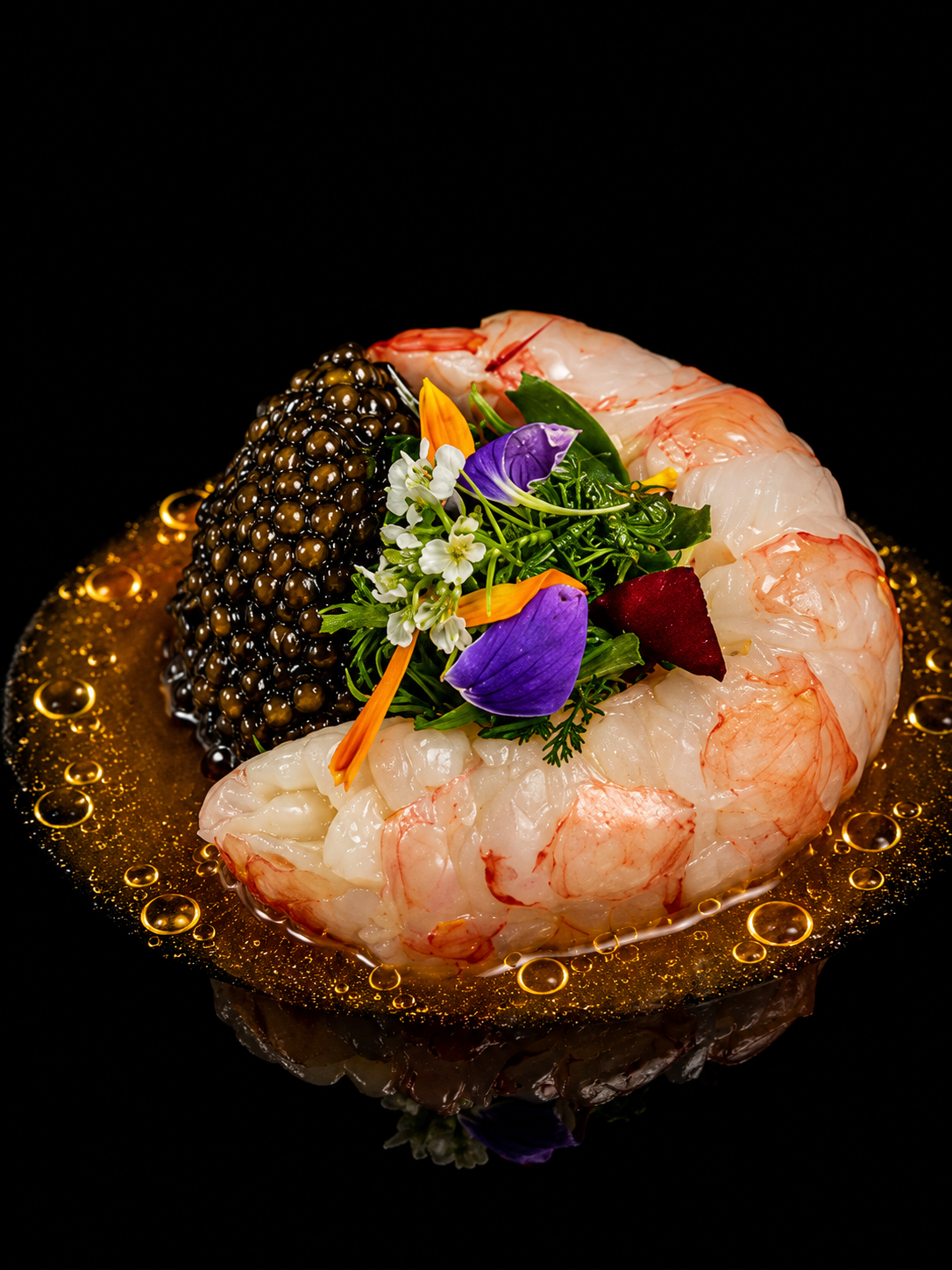 Gambas crues entourées de caviar, garnies de fleurs comestibles et d'herbes aromatiques, avec une sauce ou un coulis doré