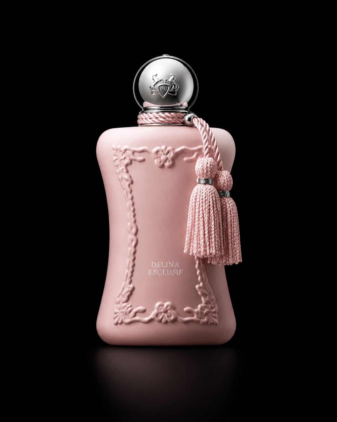 Flacon de parfum rose pastel avec décor sophistiqué et un bouchon argenté orné d'un logo, orné d'une cordelette avec des pompons. Sur le flacon, il est écrit "DELINE EXCLUSIF".