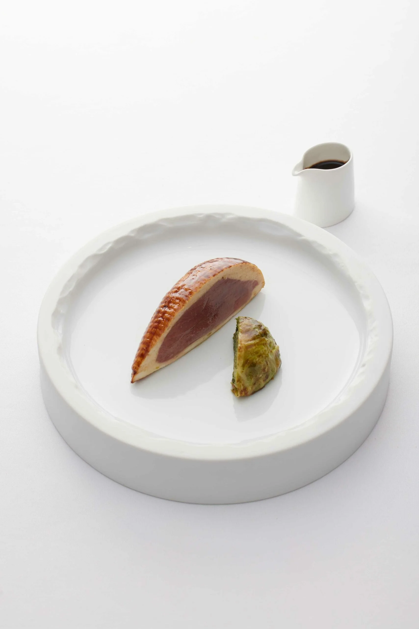 Une assiette blanche avec un morceau de foie gras et une figue.