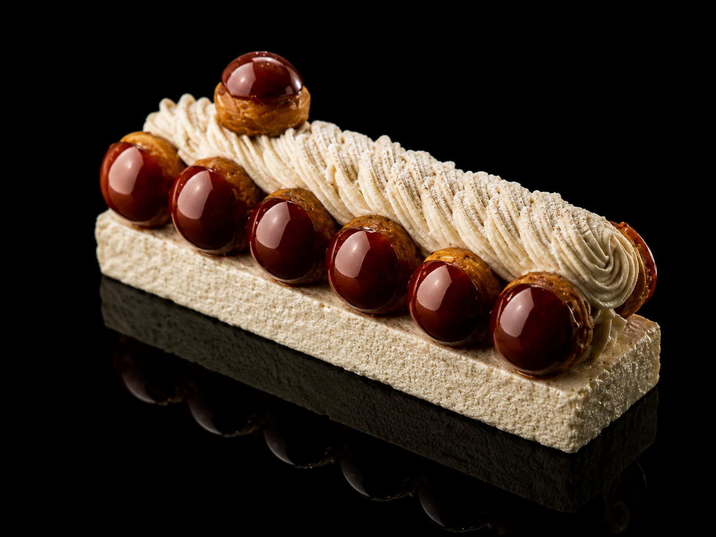 Dessert rectangular avec des choux au caramel et crème, décoré de boules en chocolat brillant, sur fond noir