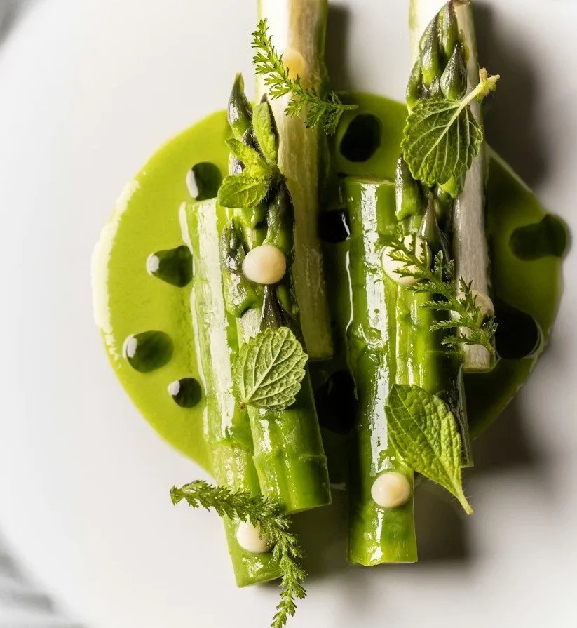 Assiette de légumes verts : asperges, courgettes et un cercle de purée de pois verts, garnis de feuilles de menthe, de petits morceaux de crème ou de fromage, et de points de sauce foncée.