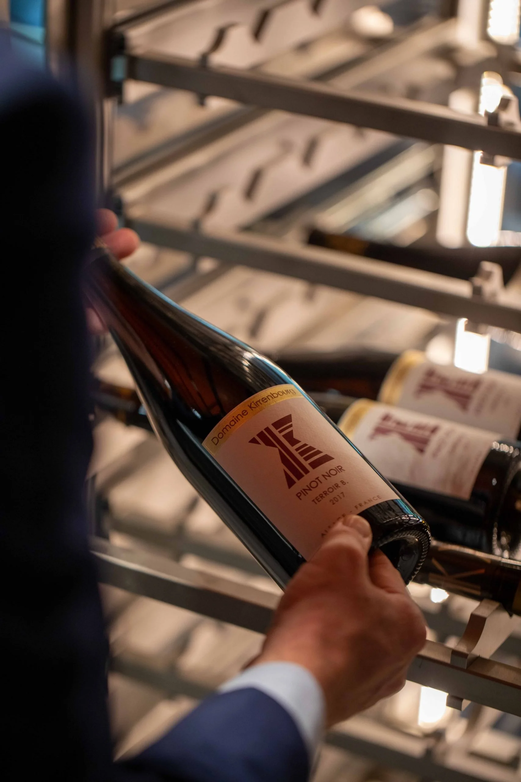 Une personne tient une bouteille de vin rouge dans une cave à vin.