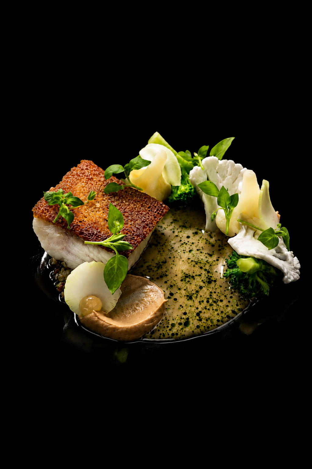Assiette de poisson avec légumes verts, sauce verte, et garnitures végétales sur un fond noir.