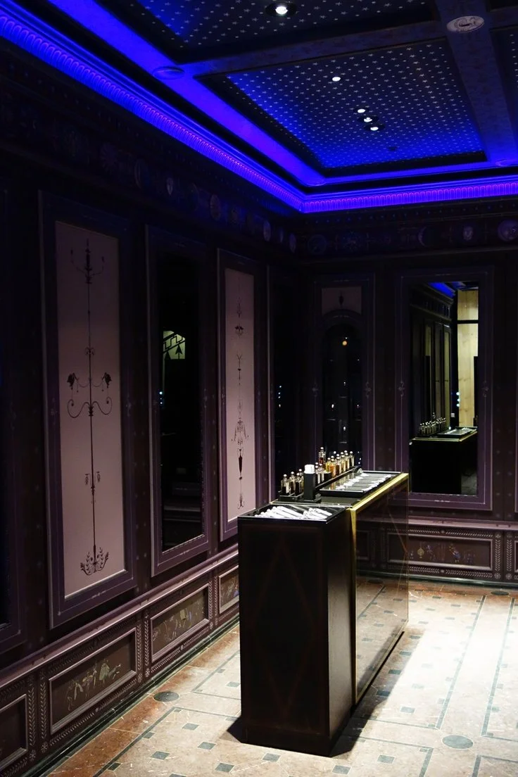 Une pièce sombre avec un panneau de présentation de parfums et un plafond illuminé en bleu dans un décor élégant et luxueux.