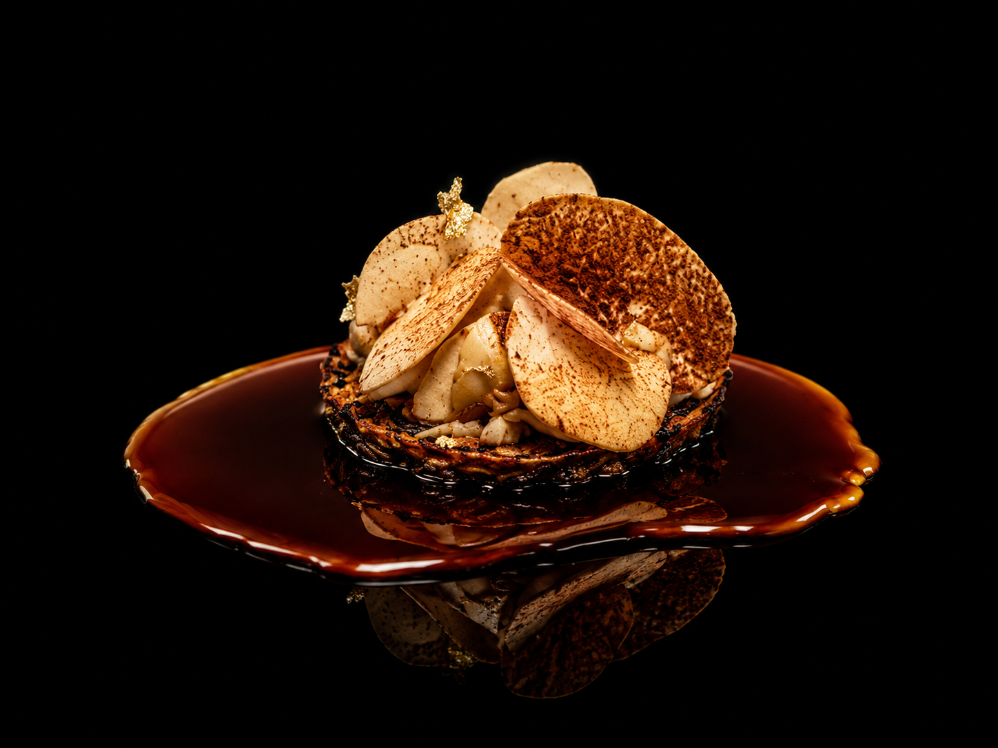 Dessert à base de pommes tranchées, de chocolat et de caramel, présenté sur une assiette en céramique, avec un fond noir.