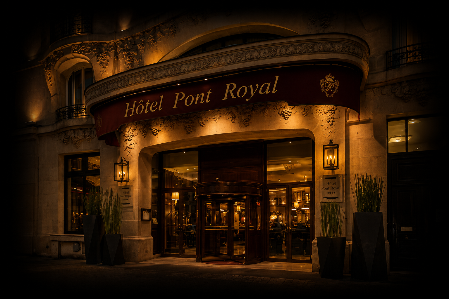 Entrée de l'Hôtel Pont Royal illuminée la nuit, façade en pierre avec un auvent rouge et or, décorations florales sculptées, lumières chaleureuses, grandes vases avec des plantes