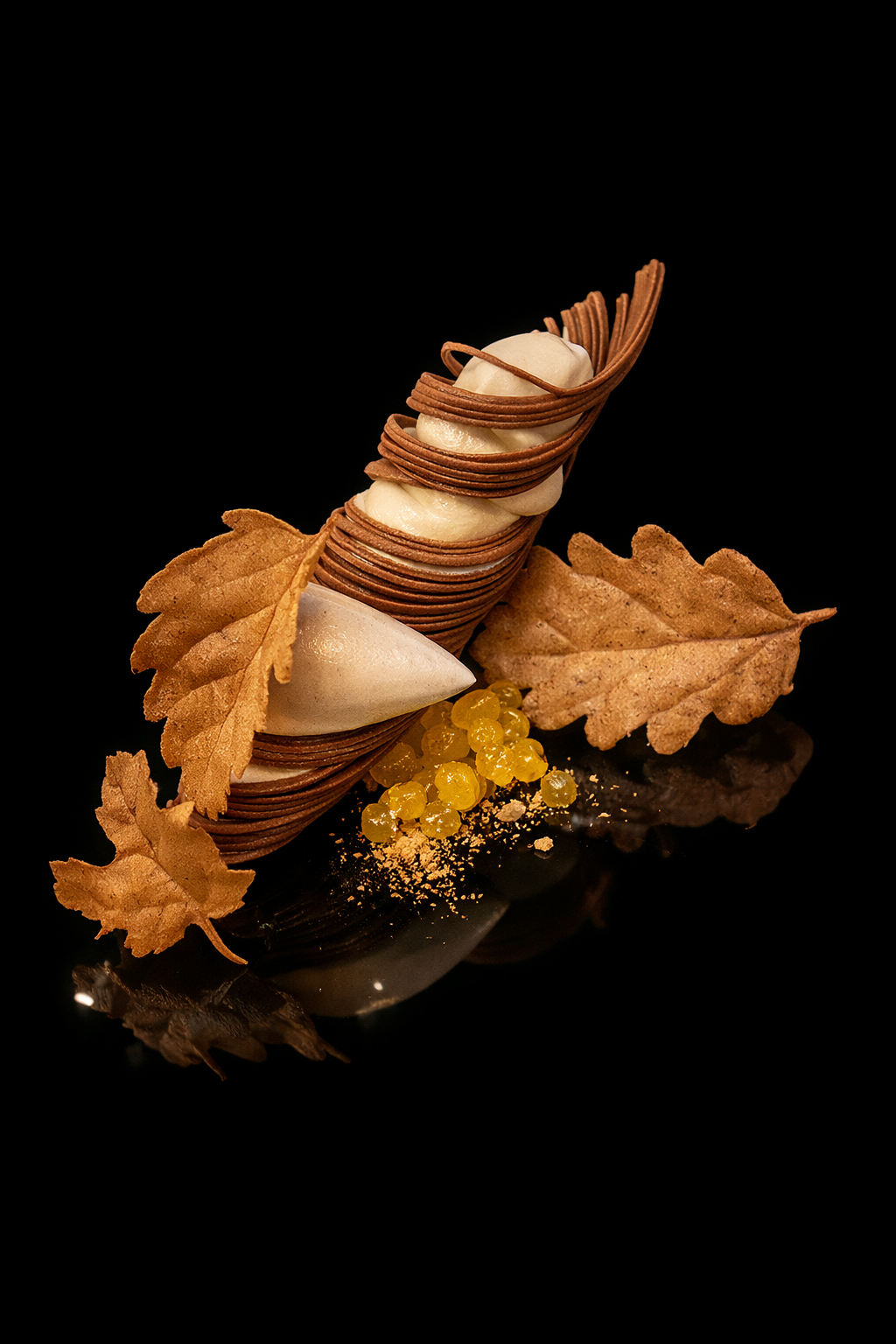 Dessert sophistiqué composé de couches de biscuits fins enroulés, de crème blanche, de feuilles enroulées, de petites perles jaunes, et décoré avec des feuilles d'automne en ardoise noire.