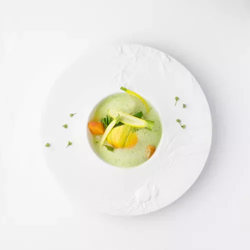 Assiette élégante avec une soupe verte garnie de légumes colorés, présentée dans un bol blanc abstrait