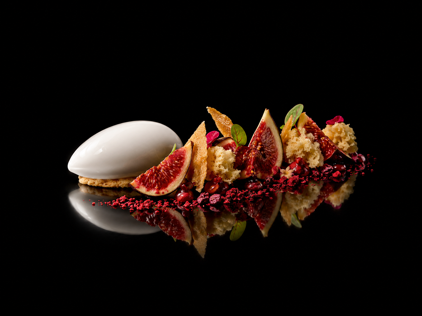 Dessert sophistiqué avec des morceaux de figues fraîches, un sorbet blanc, des feuilles vertes, des éclats de biscuit, des baies rouges, et des accessoires décoratifs sur une surface noire reflétante.