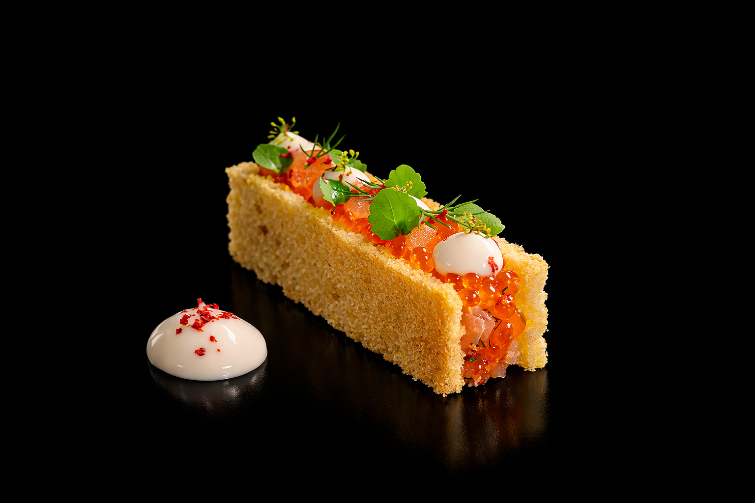 Une tranche de gâteau salé garnie d'œufs de saumon, de caviar, de feuilles de verdure et accompagnée d'une sauce blanche avec des épices rouges, sur un fond noir.