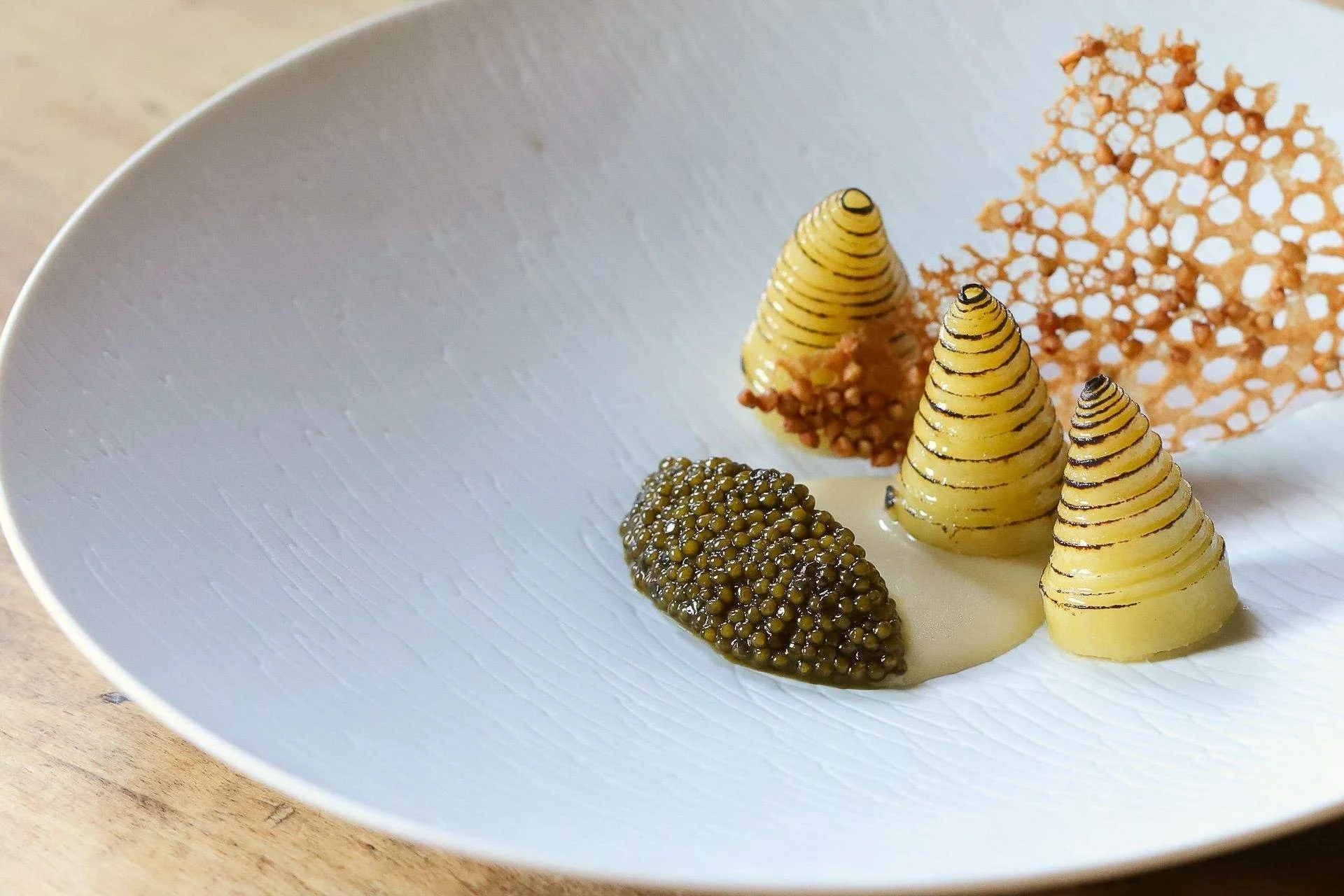 Assiette blanche avec des spirales de fromage de couleur claire, de la gelée noire, une couche de sauce blanche et une fine couche de croustillant orange gépvoudé.