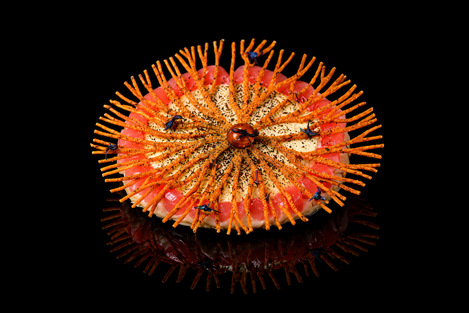 Gâteau décoré avec des tiges orange en forme de rayons, des perles de gelée rose, un glaçage blanc, des graines noires, et des insectes en plastique ou en sucre sur un fond noir