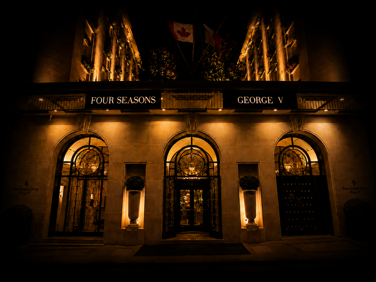 Vue nocturne de l'hôtel Four Seasons à George V avec enseignes lumineuses et drapeaux au sommet, façades éclairées dans un style élégant.