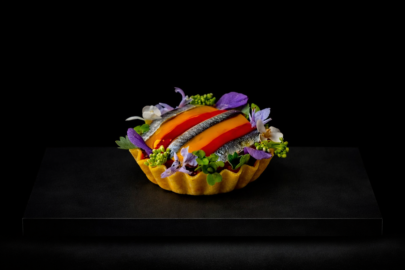 Tartelette salée avec des filets de sardines, des tranches de poivron rouge et jaune, décorée de fleurs et de feuilles