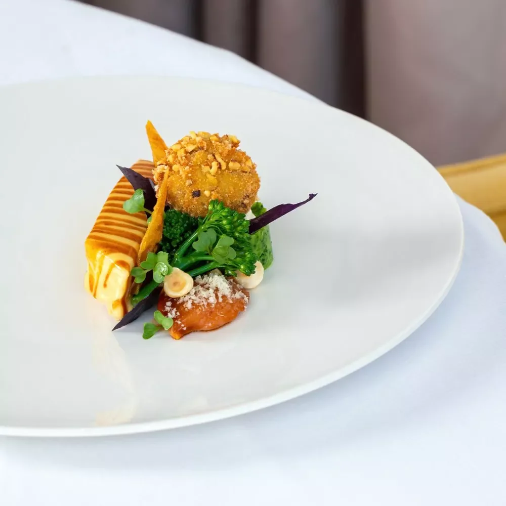 Assiette avec un aliment croustillant, des légumes verts, un filet de sauce et décoration végétale.
