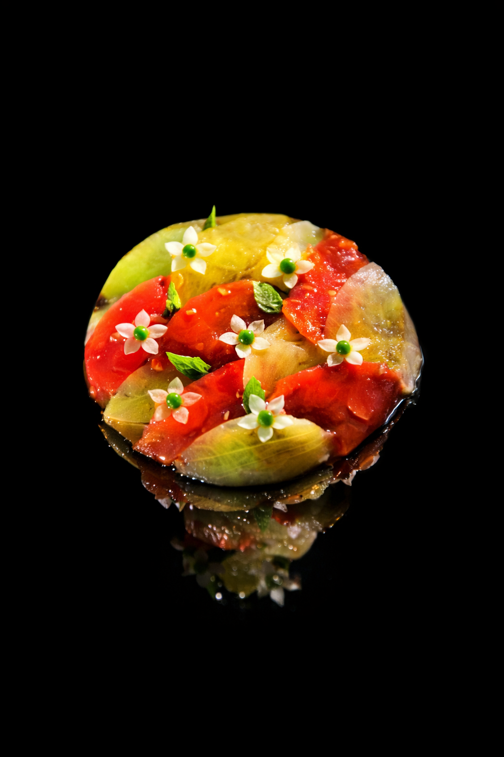 Une pâtisserie décorée avec des morceaux de fruits colorés, des fleurs blanches et des feuilles vertes, sur un fond noir.