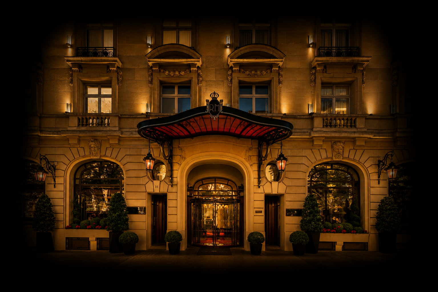 Façade d'un hôtel élégant éclairée la nuit, avec un auvent noir et rouge, des lampes suspendues, des fenêtres avec rideaux et des plantes en pots.