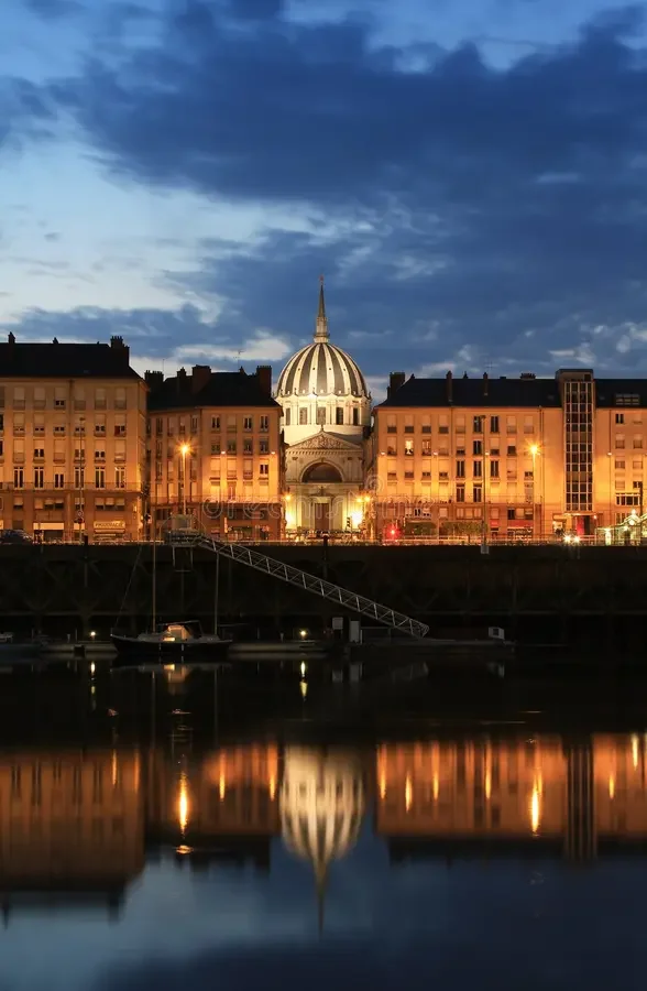 Vue d'une ville avec un bâtiment en forme de dôme au centre, reflet dans l'eau en premier plan, ciel orageux au-dessus.