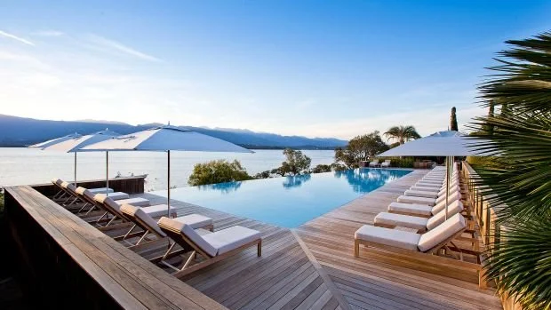 Piscine à débordement avec des chaises longues et parasols, vue sur un lac ou un océan, avec des montagnes en arrière-plan