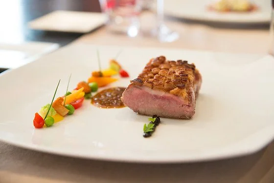 Steak de viande rose servi avec une garniture de sauces et légumes colorés sur une assiette blanche.