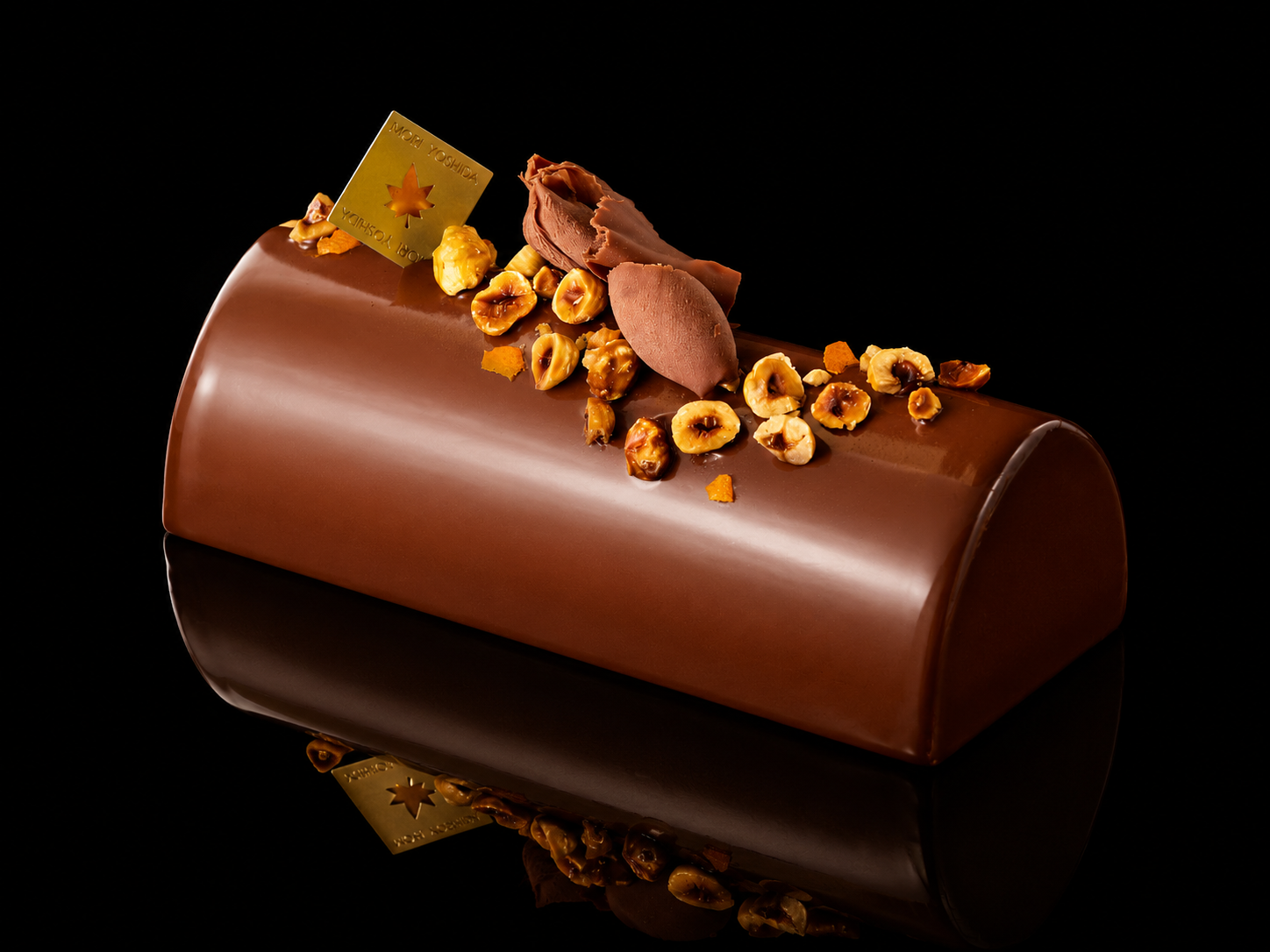 Gâteau glacé au chocolat décoré de noisettes, de chocolat et d'une plaque en or avec une étoile, posé sur fond noir