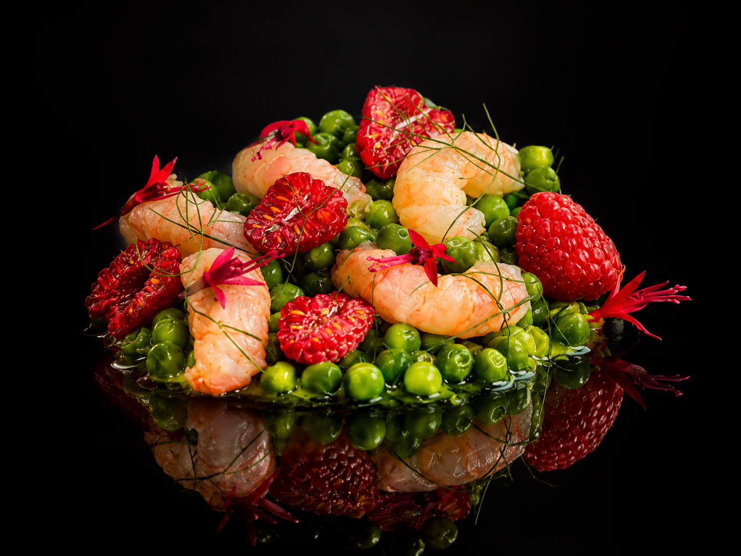 Assiette de crevettes, fraises, groseilles, pois verts, décorations florales sur fond noir.