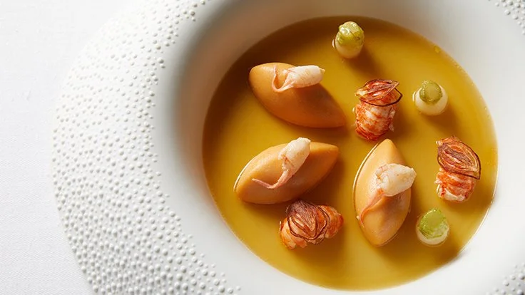 Soupe avec palourdes, crevettes, petits légumes et bouillon clair dans un bol blanc.