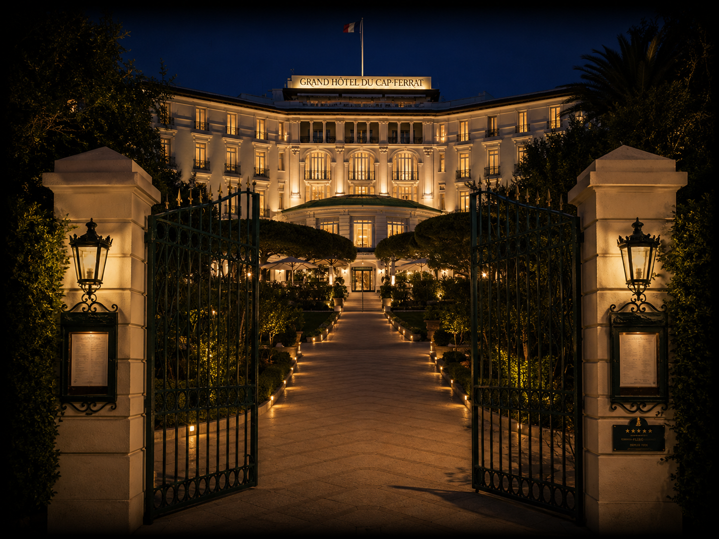 Un grand hôtel élégant éclairé la nuit, vu à travers une porte entrouverte avec un chemin lumineux menant à l'entrée principale.